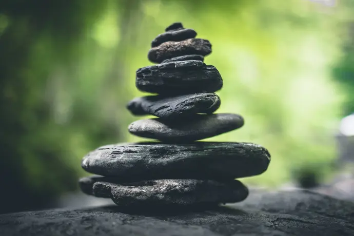 Empilement de pierres zen noires en équilibre (cairn) sur fond de forêt verte floue, symbolisant l'harmonie, l'équilibre des chakras et la sérénité.